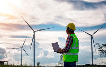 Engineering man standing holding laptop looking wind turbines clean energy project for produce electricity and checking wind direction